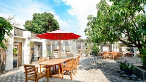 An outdoor patio with a wooden table and chairs, a red umbrella, and potted plants. - OYO 2327 Pagsis Village (Klaten)