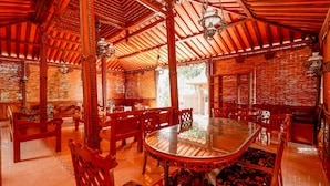 A traditional wooden dining area with a round glass table surrounded by ornate chairs, featuring intricate woodwork and a high ceiling with exposed beams. - OYO 2327 Pagsis Village (Klaten)
