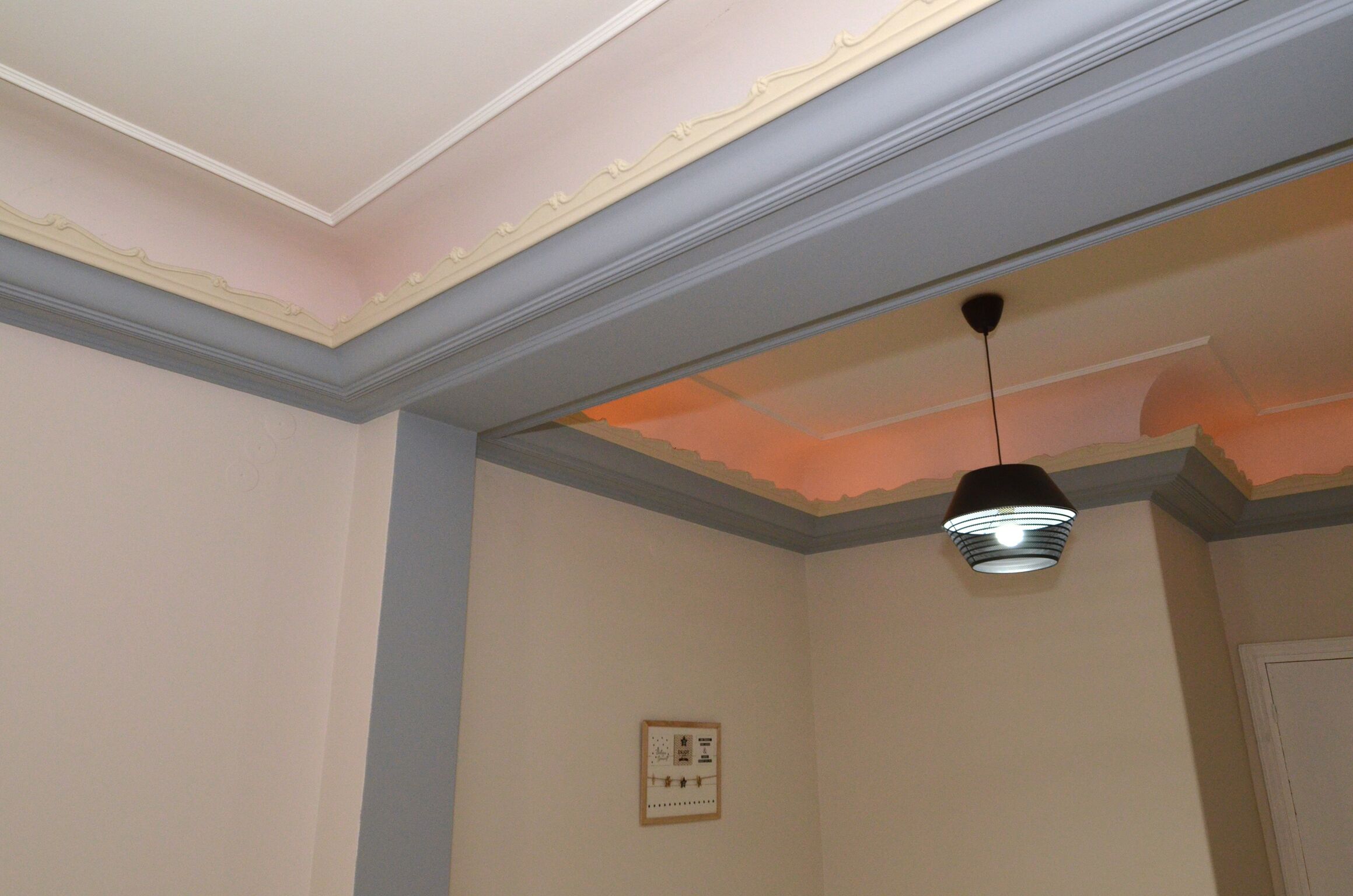 Una habitación con techo de molduras decorativas y una lámpara colgante.