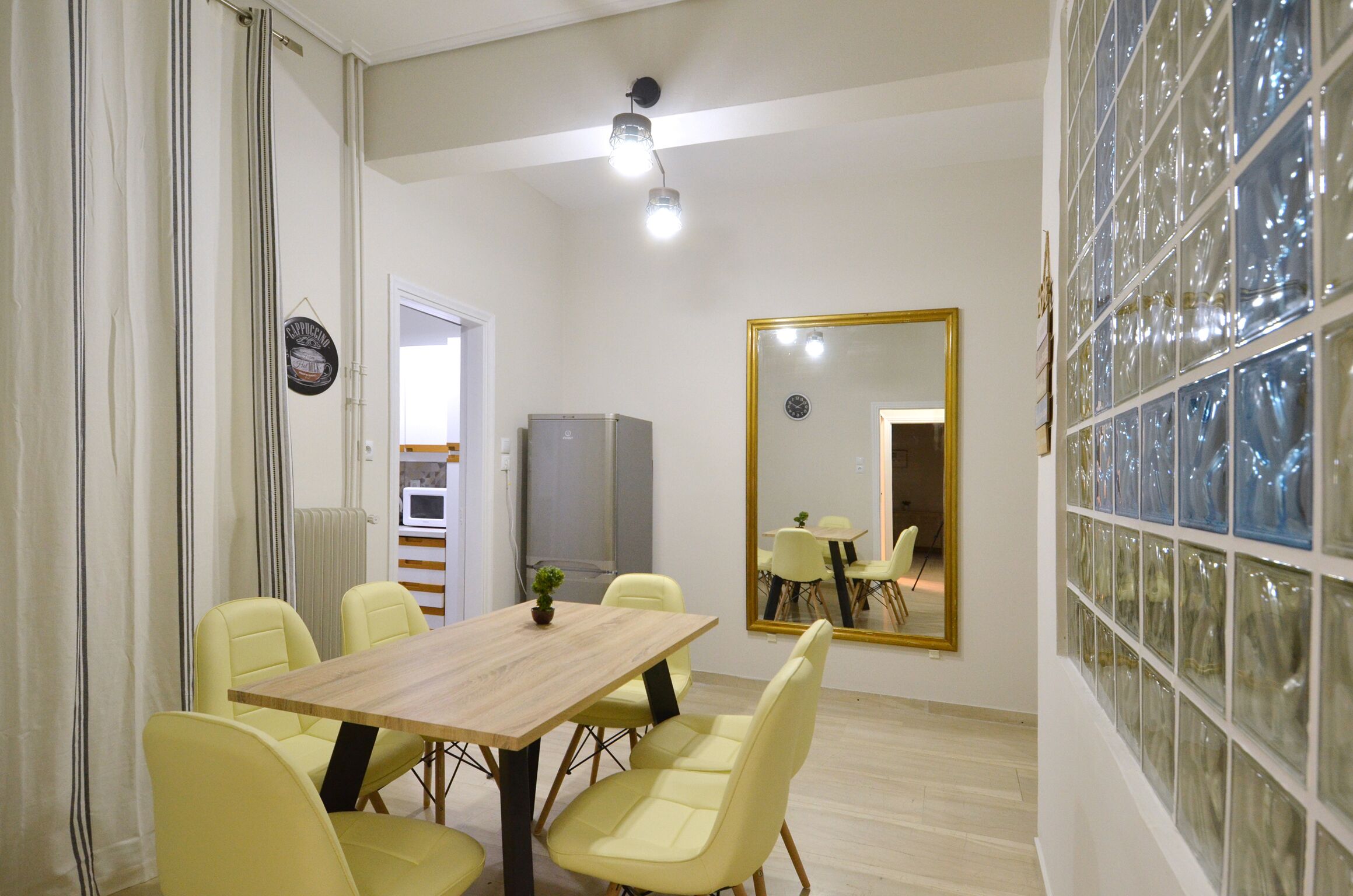 A dining area with a wooden table and yellow chairs, a large mirror, and a view of a window with glass blocks.
