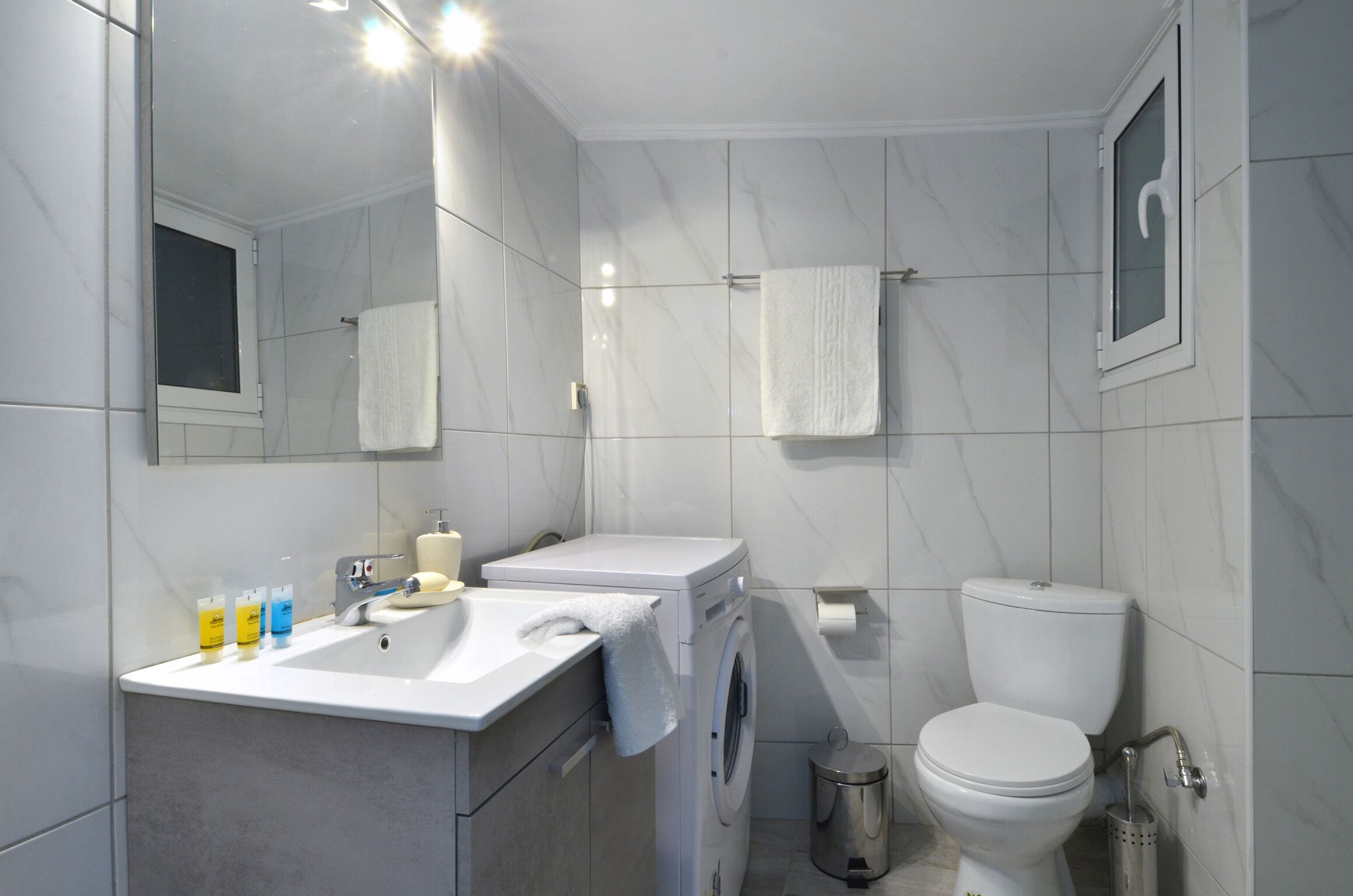 A modern bathroom with a sink, mirror, towel rack, toilet, and a trash bin.