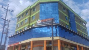 A multi-story building with a green and blue facade, featuring a sign for 'Moonshine Discottique' and 'Trinity Hardware' on the ground floor. - Moonshine Walkers (Eldoret)