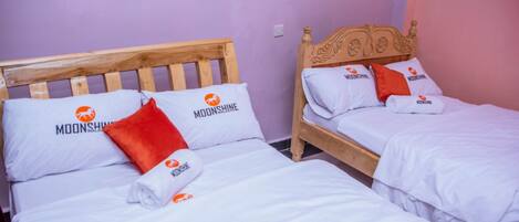 Two twin beds with wooden headboards, white bedding, and orange pillows with the Moonshine logo.
