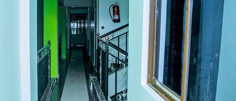 A hallway with a green accent wall, a fire extinguisher mounted on the wall, and a window with a decorative frame.