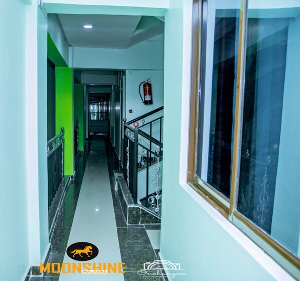 A hallway with a green accent wall, a fire extinguisher mounted on the wall, and a window with a decorative frame.