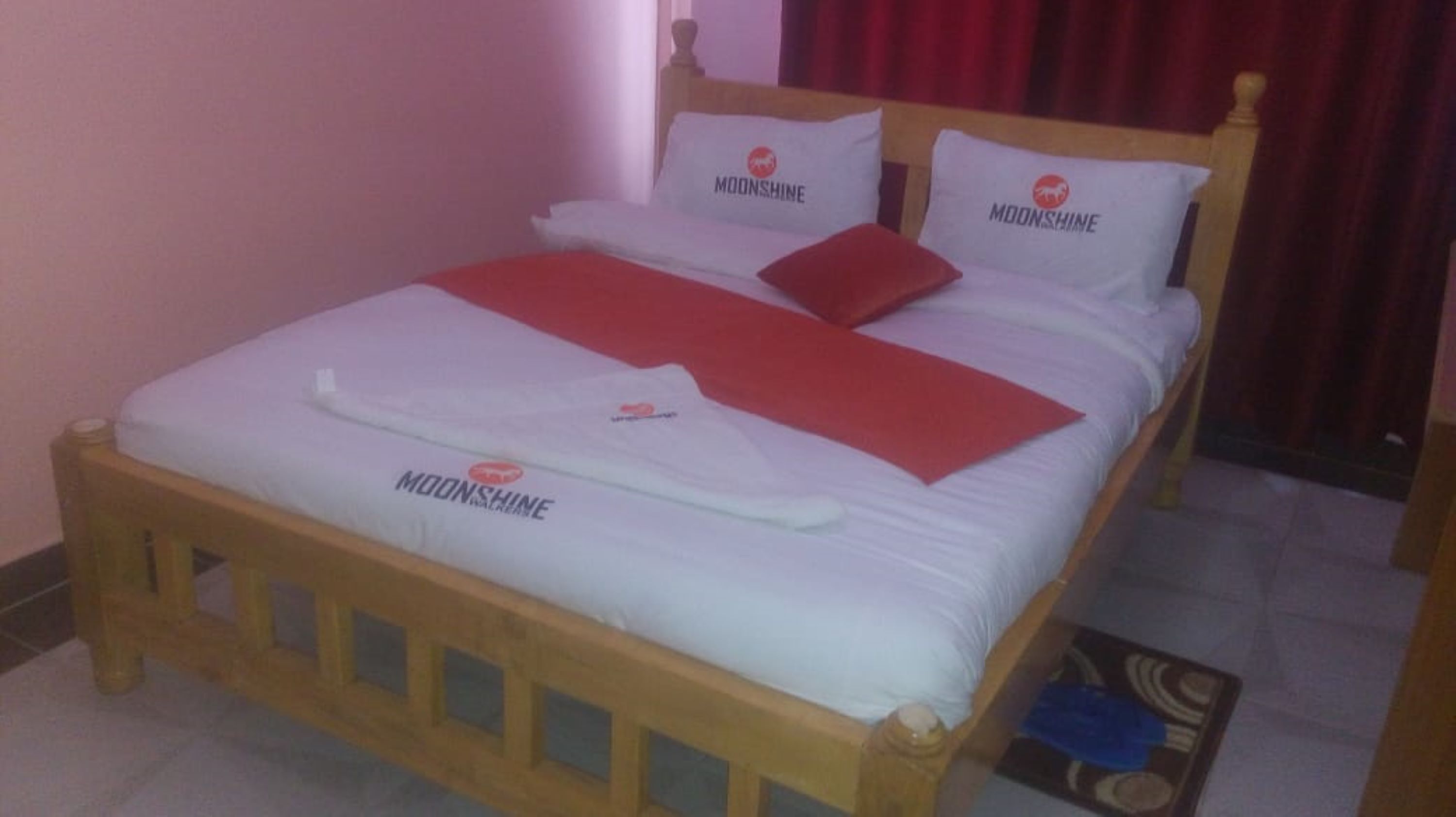 Una cama con estructura de madera, ropa de cama blanca y almohadas con el logo 'Moonshine'.