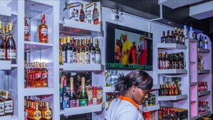 A liquor store with shelves stocked with various bottles and a television screen displaying an advertisement. - Moonshine Walkers (Eldoret)