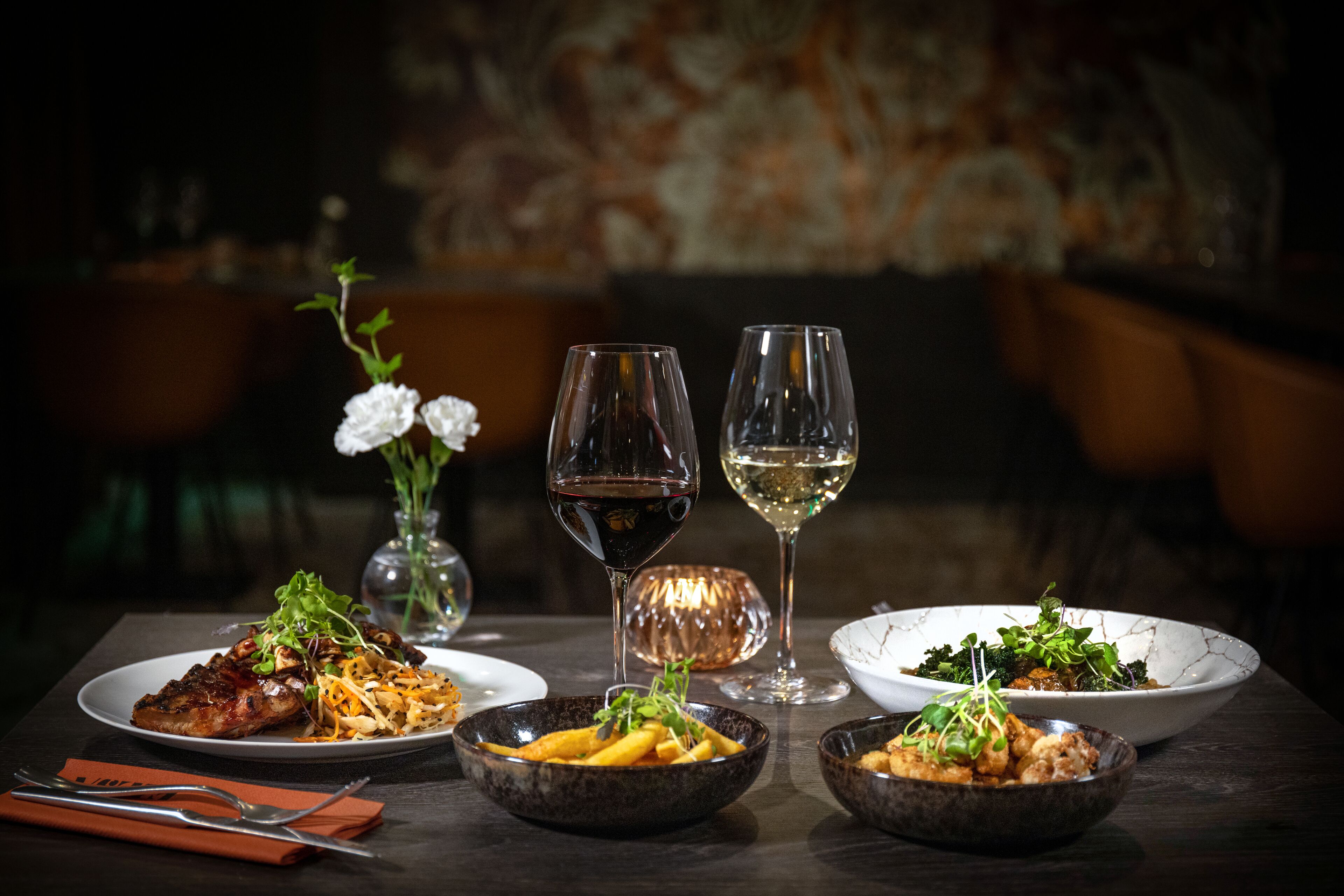 Une table à manger avec différents plats, des verres de vin et un vase rempli de fleurs.