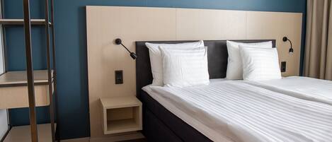 Ein ordentlich gemachtes Bett mit weißen Leinentüchern, einem Holzkopfteil und einem Nachttisch mit Lampe.