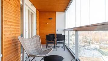 A balcony with a wicker chair and a small table, wooden panel walls, and a view of a snowy landscape.