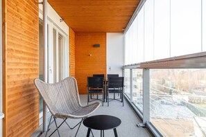 A balcony with a wicker chair and a small table, wooden panel walls, and a view of a snowy landscape. - Hotel Matts (Espoo)