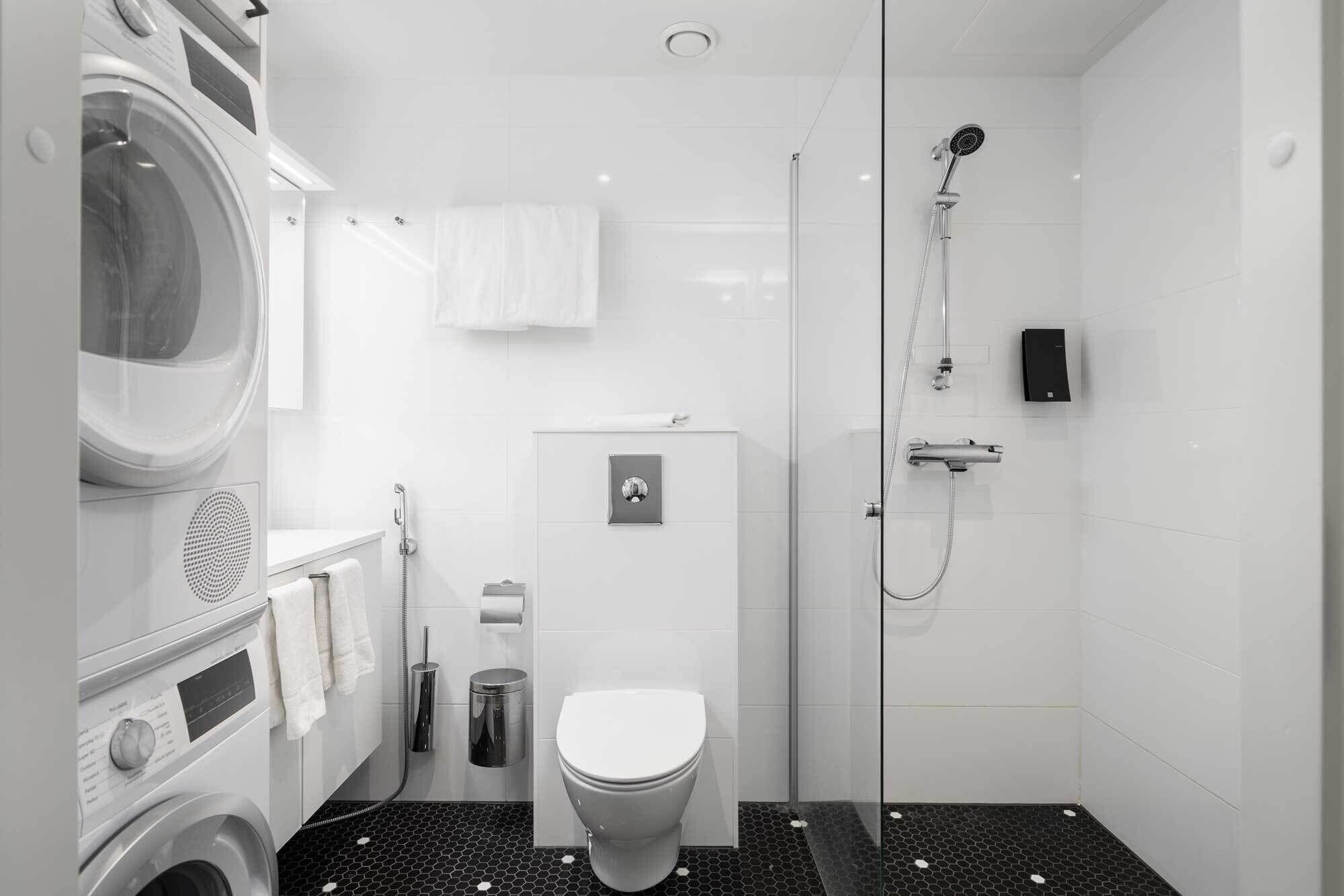 A compact, modern bathroom with a washing machine, toilet, and glass-enclosed shower area.