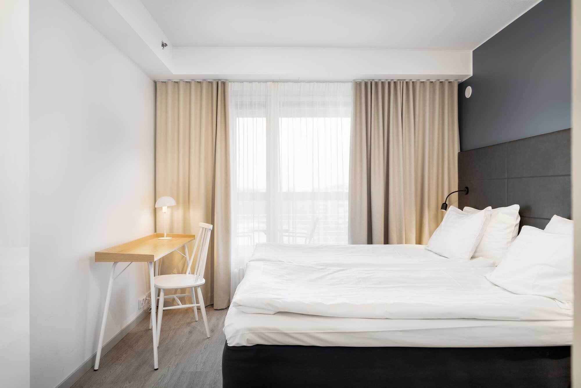 Een hotelkamer met een bed, een bureau, een stoel en een raam met gordijnen.