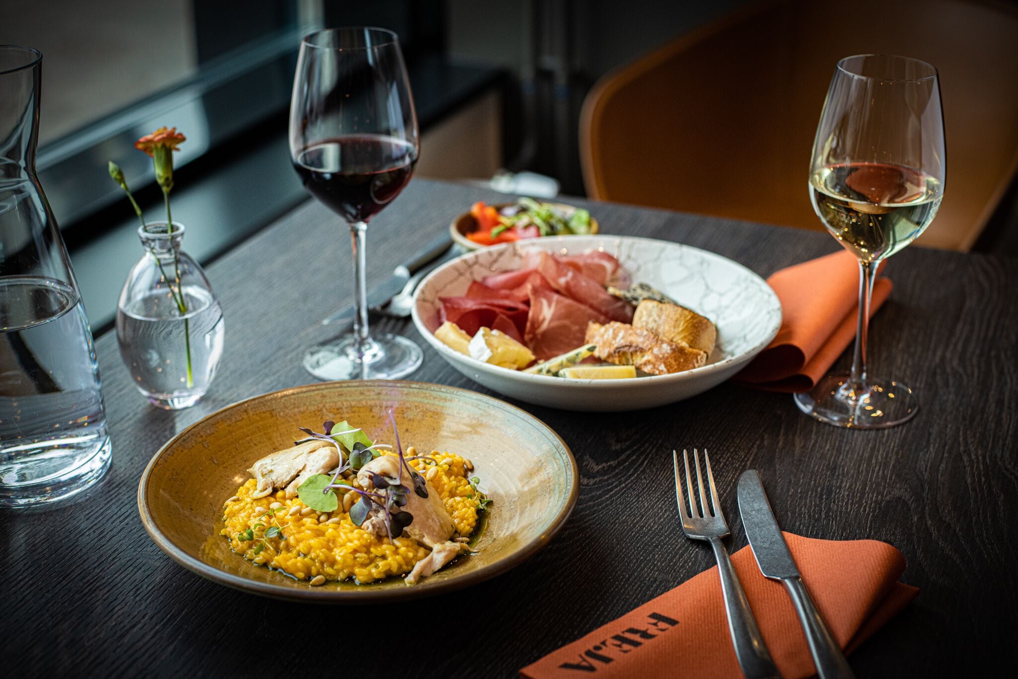 Una mesa de comedor con platos de comida, copas de vino y cubiertos.