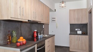 Moderni keittiö, jossa on puiset kaapit, sisäänrakennettu uuni ja työtaso, jonka päällä on hedelmiä ja vedenkeitin.