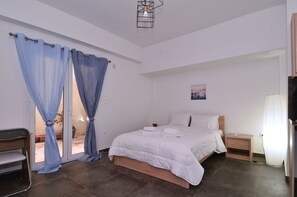 A bedroom with a bed, a nightstand, a chair, and a window with curtains. - Koukaki a minimal studio (Athens)