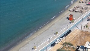 Luchtbeeld van een strand met een weg langs de kust, een redershut en strandparasols.