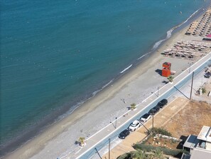 Ein Luftbild eines Strandes mit einer parallel zur Küste verlaufenden Straße, einem Rettungsturm und Strandstühlen.