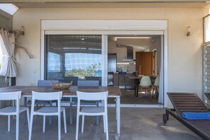 Comedor con mesa y sillas, cocina al fondo y puerta corrediza de vidrio que da a un patio.