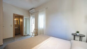 Hotelkamer met een bed, een klein tafeltje met een plant, een badkamer met een spiegel en een airconditioning.