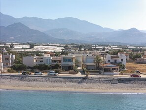 Un área residencial costera con edificios, una playa y montañas al fondo.