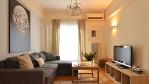 A living room with a sofa, a coffee table with a vase, a television on a wooden stand, and an air conditioning unit on the wall. - Exarchia a nice and cozy apartment (Athens)