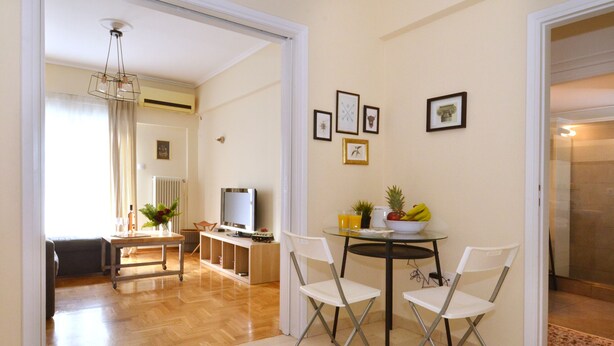 A spacious living area with a dining table, two chairs, a television, and a kitchen area in the background. - Exarchia a nice and cozy apartment (Athens)