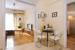 Amplia sala de estar con una mesa de comedor, dos sillas, un televisor y una zona de cocina al fondo.