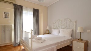 A neatly made bed with white linens, a bedside table with a lamp, and a radiator. - Exarchia a nice and cozy apartment (Athens)