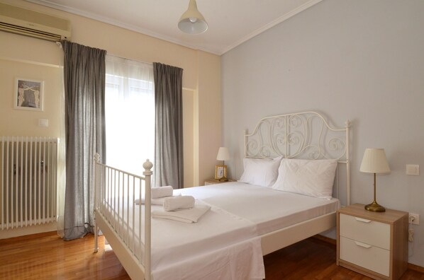 Una cama bien hecha con ropa blanca, una mesita de noche con lámpara y un radiador.
