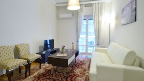 A living room with a sofa, two armchairs, a coffee table, a TV, and a window with curtains. - Niovis a nice and cozy apartment (Athens)