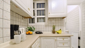 A kitchen with white cabinets, a coffee maker, a fruit bowl with bananas and oranges, and a plant. - Niovis a nice and cozy apartment (Athens)