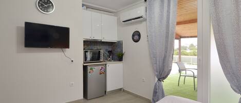 Ein Schlafzimmer mit Bett, Fernseher, Küchenzeile und einem Balkon mit Vorhängen.
