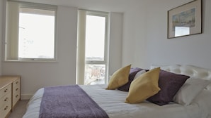A bedroom with a bed, two windows, a dresser, and a framed picture on the wall. - Toothbrush Apartments Waterfront - Adults Only (Ipswich)