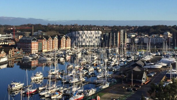 A marina with numerous boats docked, surrounded by buildings including a distinctive red brick structure and modern architecture. - Toothbrush Apartments Waterfront - Adults Only (Ipswich)