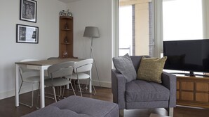 A modern living room with a grey sofa, a television, and a dining area with a table and chairs. - Toothbrush Apartments Waterfront - Adults Only (Ipswich)