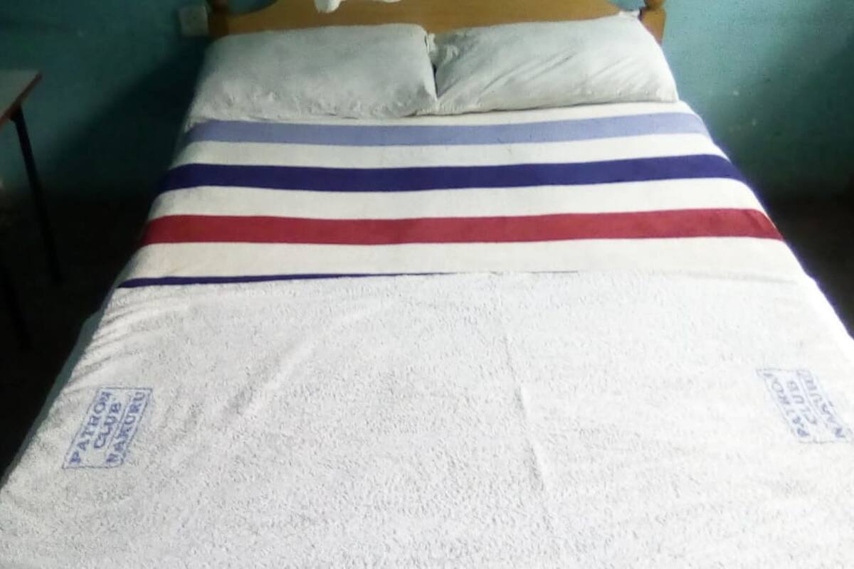 A bed with a striped bedspread and pillows, a wooden headboard, and a green wall.