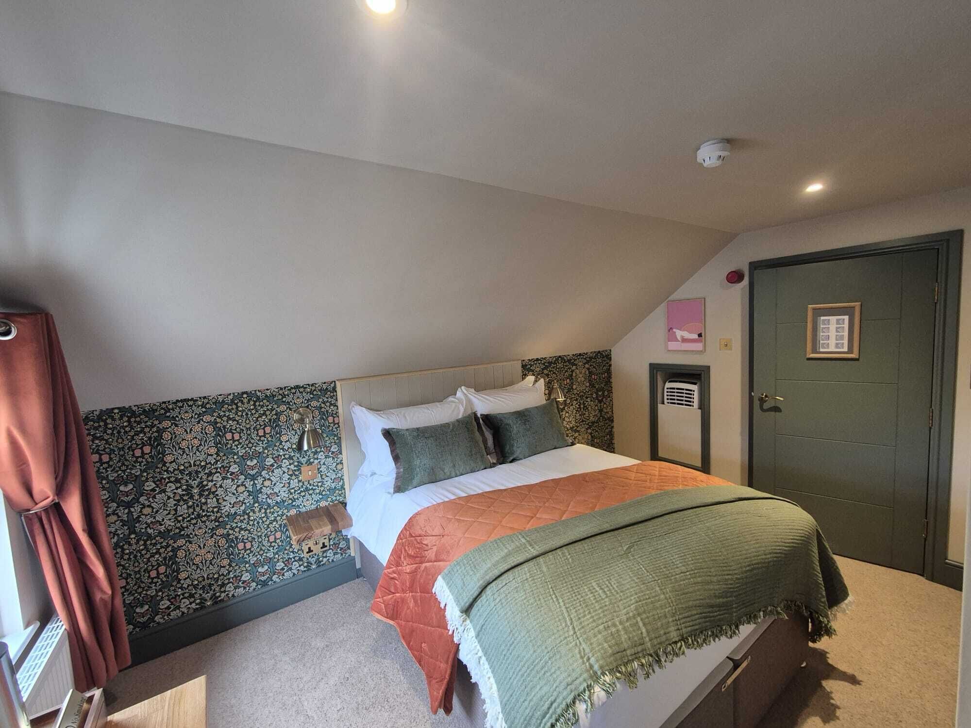 Une chambre à coucher avec un lit, une porte, un radiateur et un mur orné d’un motif floral.