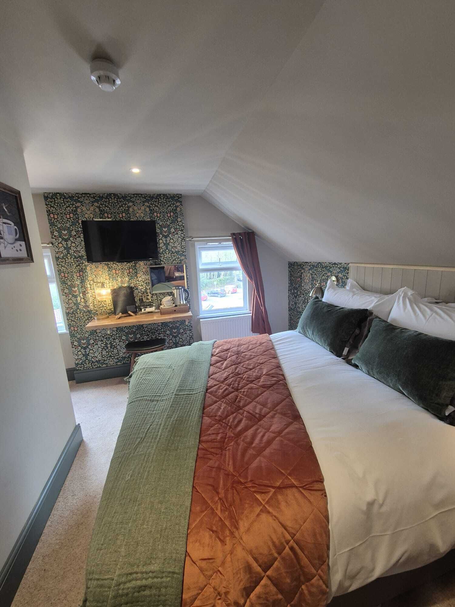 A bedroom with a bed, a desk, a TV, and a window with curtains.