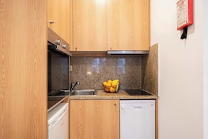 A compact kitchen with wooden cabinets, a granite countertop, a dishwasher, and a sink.