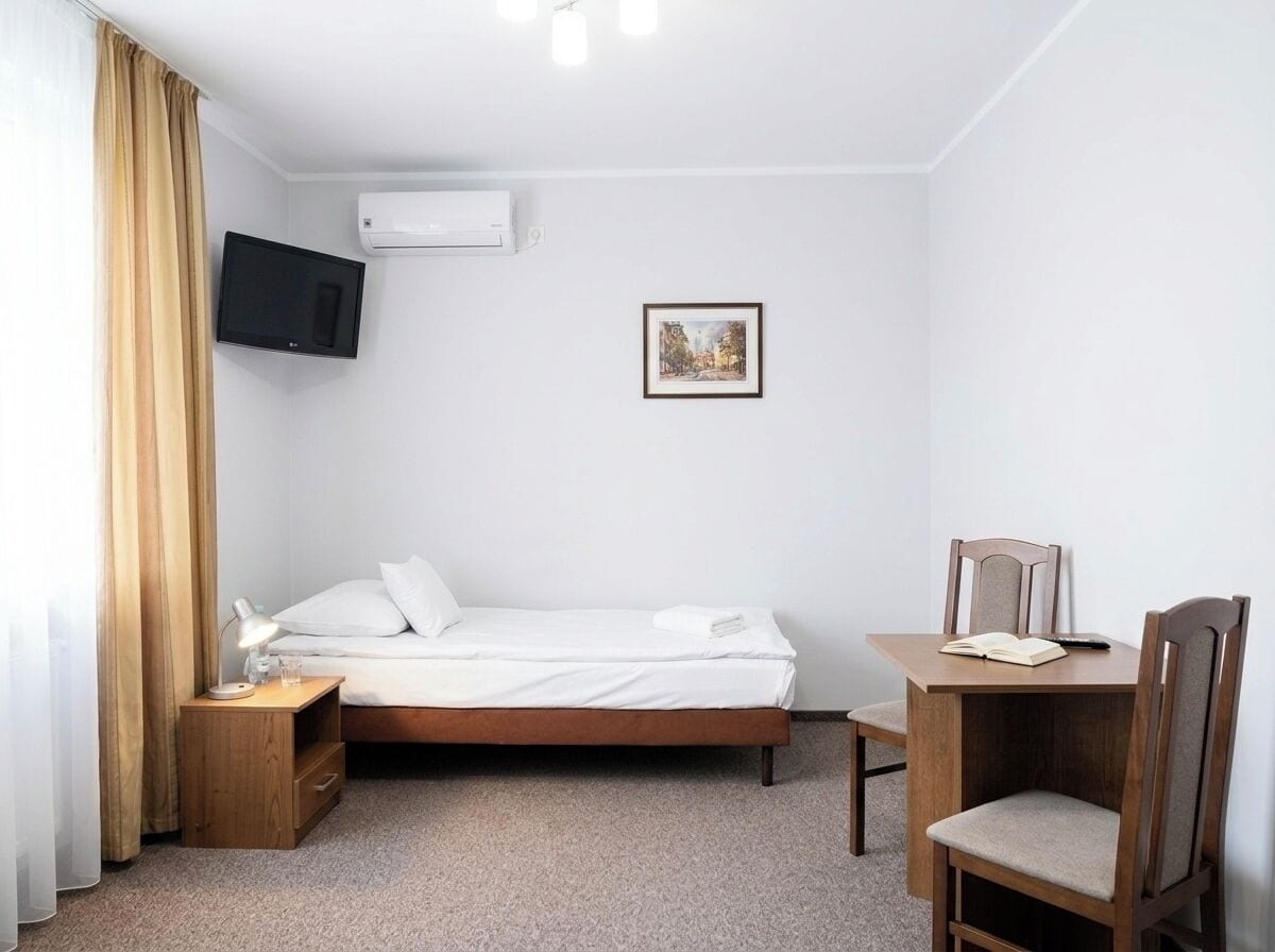 Une chambre d’hôtel avec un lit, un bureau, une chaise, une télévision, un climatiseur et un tableau au mur.