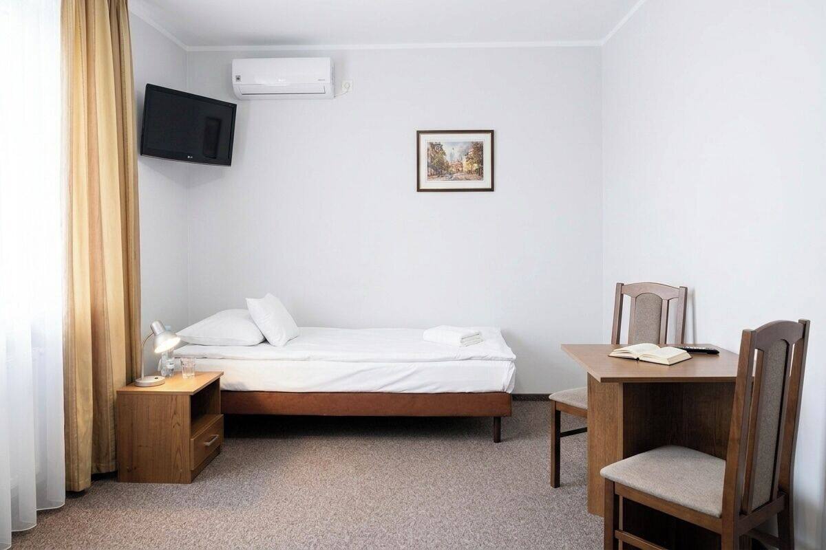 Ein Hotelzimmer mit Bett, Schreibtisch, Stuhl, Fernseher, Klimaanlage und einem Bild an der Wand.