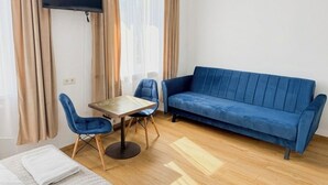 A room with a blue sofa, a small table with chairs, a TV mounted on the wall, and a bed with a white blanket. - Astral (Raszyn)