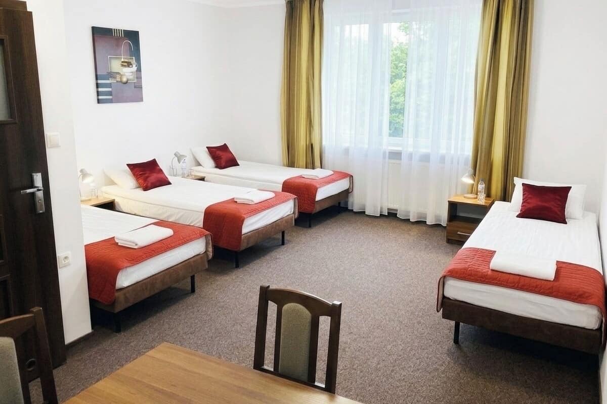 Ein Hotelzimmer mit vier Einzelbetten, einem Holztisch und einem Stuhl.