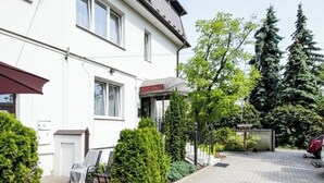 A white building with a 'Pensionat' sign, a paved driveway, and a red car parked in the background. - Astral (Raszyn)