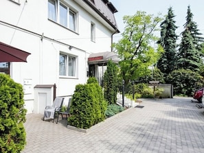 Un bâtiment blanc avec une enseigne indiquant « Pensionnat », une allée pavée et une voiture rouge garée au fond.