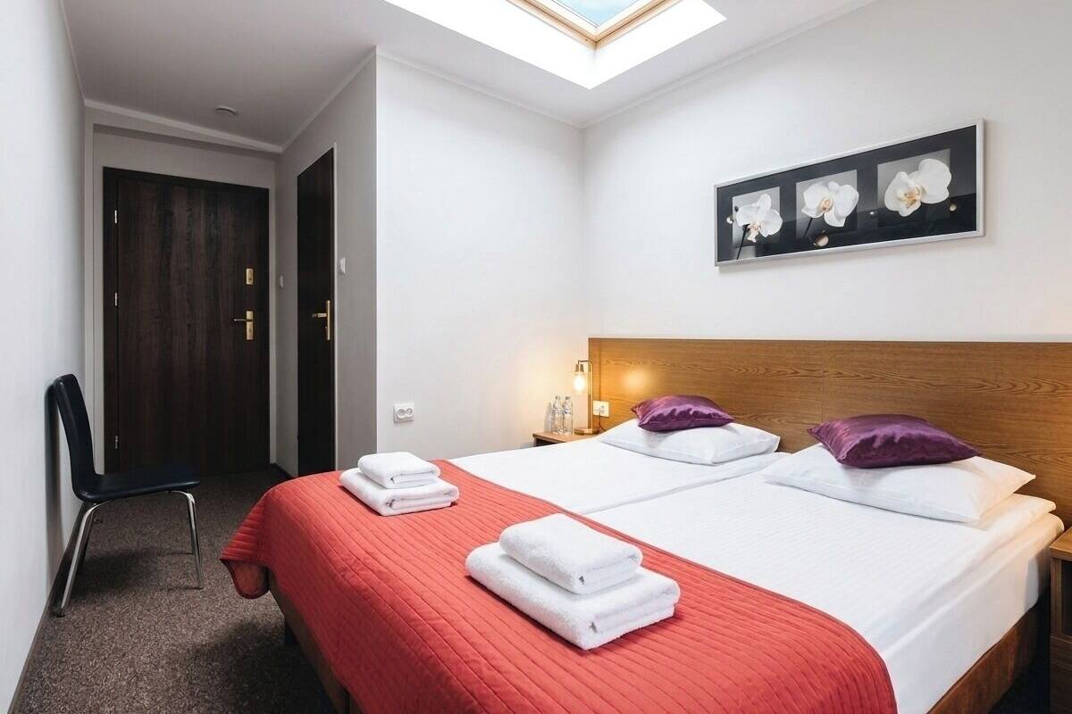 Ein Hotelzimmer mit Oberlicht, zwei Betten mit rot-weißer Bettwäsche, einem hölzernen Kopfteil, einem Nachttisch mit Lampe und einer Orchideen-Wandkunst im Rahmen.
