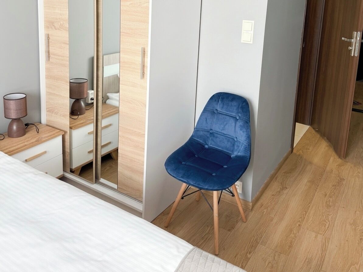A bedroom with a bed, a blue chair, a bedside table with a lamp, and a wardrobe.