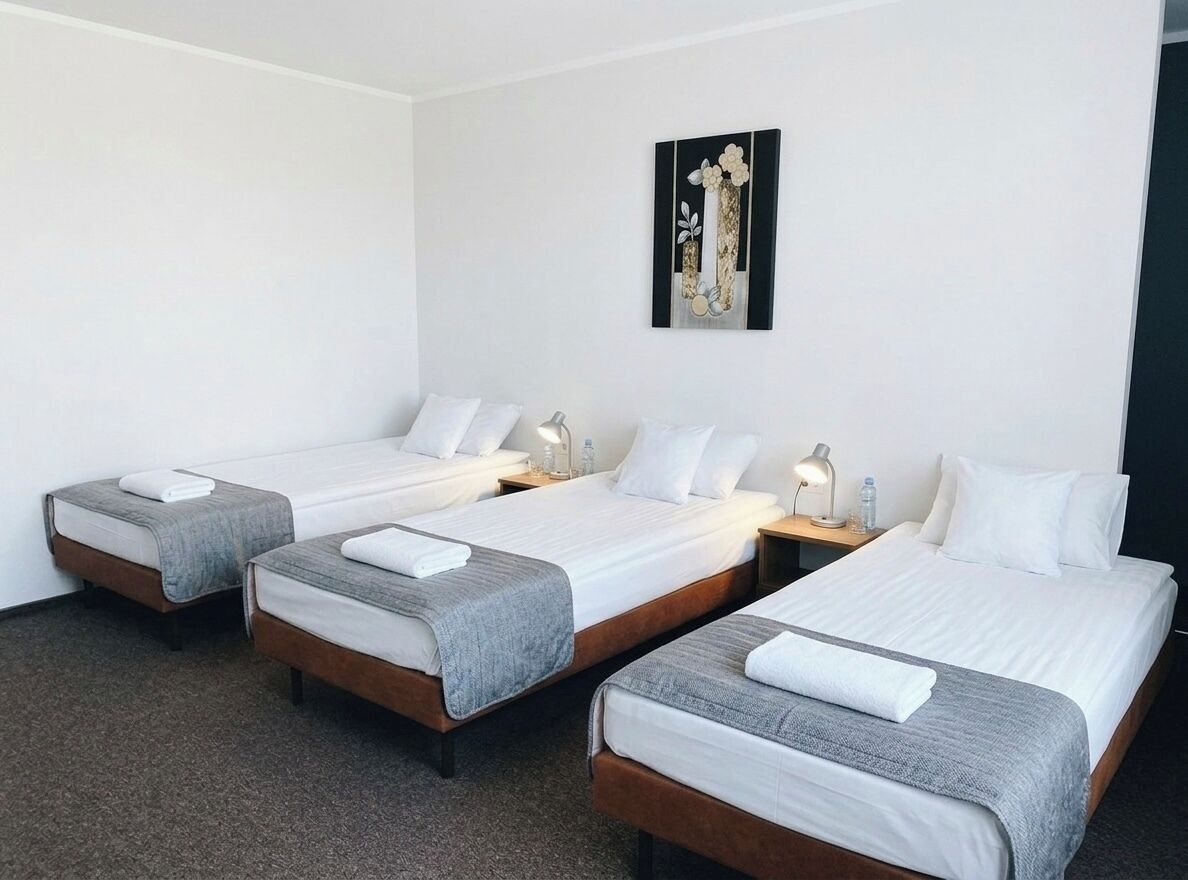 Une chambre d’hôtel avec trois lits simples, chacun étant équipé d’une table de chevet et d’une lampe.
