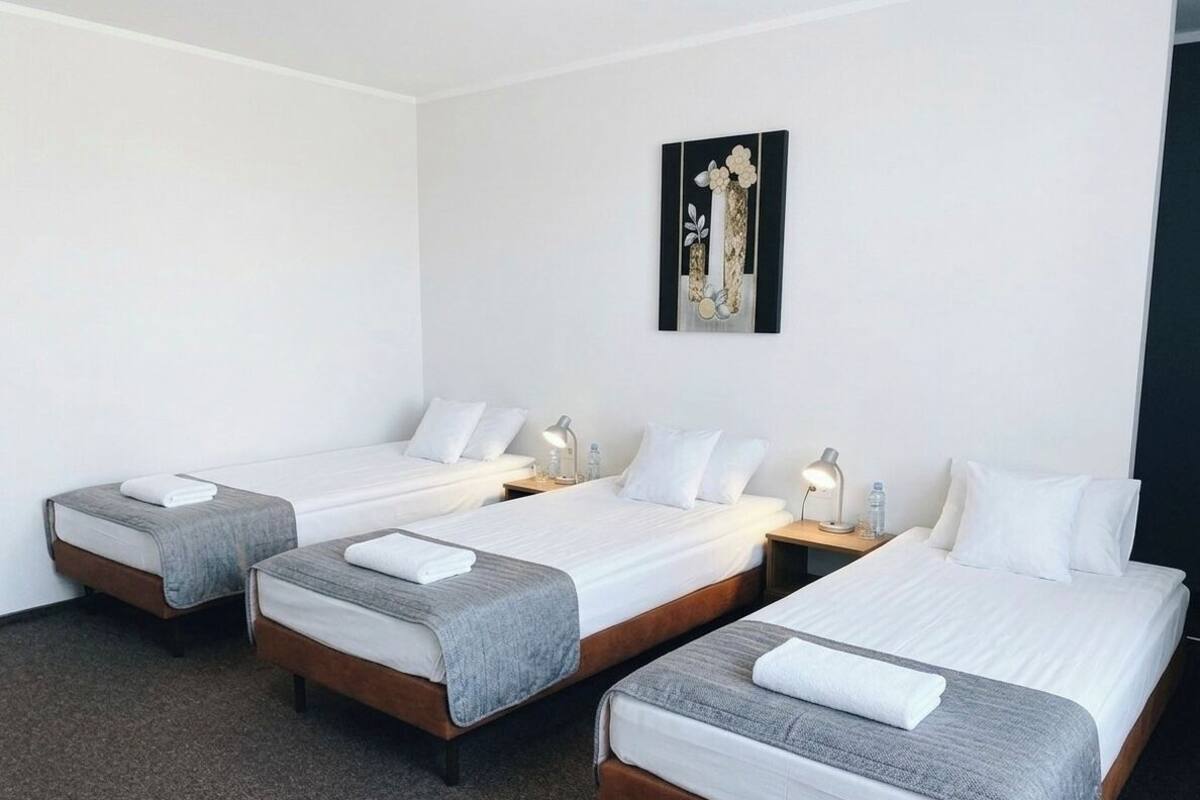 Ein Hotelzimmer mit drei Einzelbetten, jeweils mit Nachttisch und Lampe.